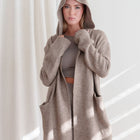 OKAKIE Adrienne heavyweight hooded cardigan in a soft beige knit with oversized hood and deep patch pockets.