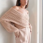 OKAKIE beige cable knit sweater featuring a crossover V-neckline and voluminous sleeves worn by a woman.