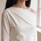 OKAKIE Solène cream scuba knit top featuring an elegant asymmetric neckline and long sleeves on a model