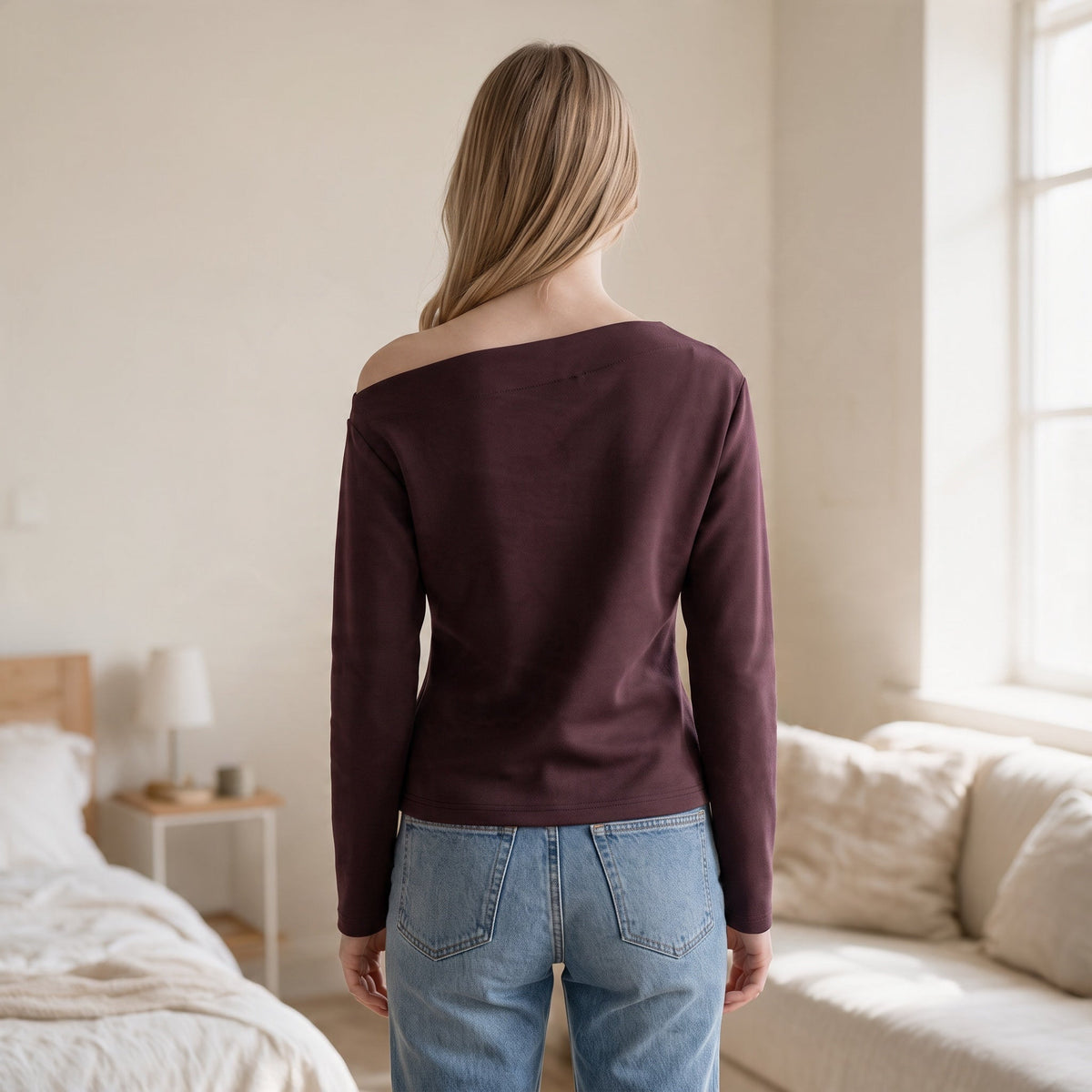 Back view of a woman wearing an OKAKIE dark plum asymmetric scuba knit top with long sleeves and off-shoulder detail.