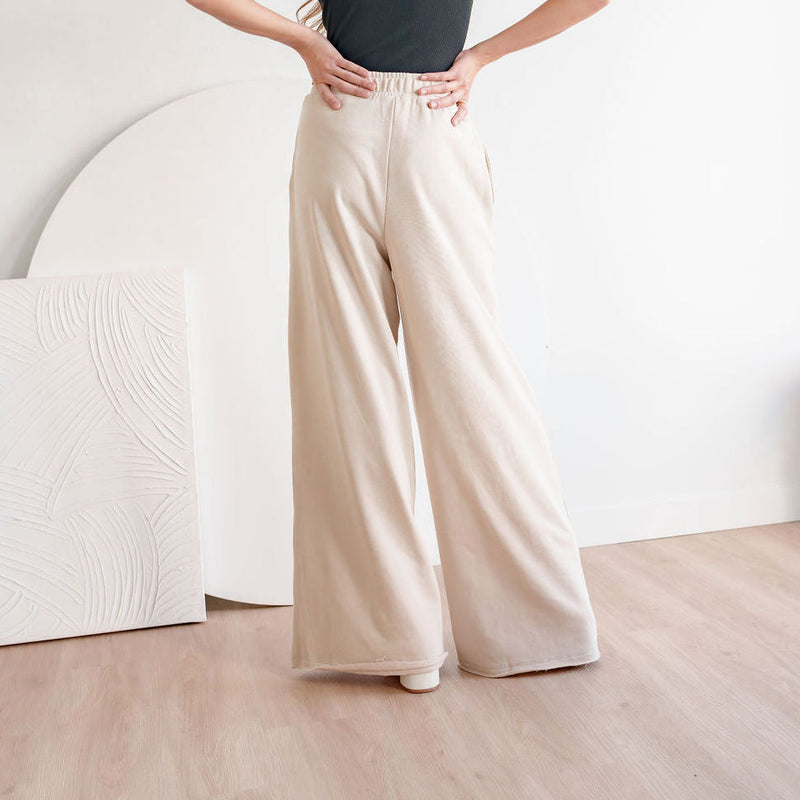 OKAKIE Aurelia beige French terry sweatpants with a high-rise elastic waist and dramatic wide-leg silhouette.