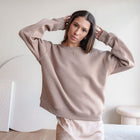 Model wearing an OKAKIE relaxed fit beige cotton fleece crewneck sweatshirt with dropped shoulders and ribbed trim.