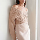 OKAKIE beige cable knit sweater with a criss-cross off-shoulder neckline and wide dolman sleeves on a model