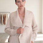 Model wearing an OKAKIE beige heavy cotton blend coatigan with an oversized lapel and thick purl knitted texture.