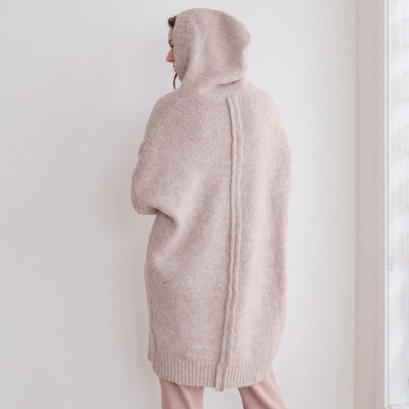 OKAKIE beige oversized hooded knit cardigan worn by a model, showing the back view with ribbed hem and textured knit.