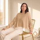 OKAKIE oversized beige purl knit cropped sweater with crew neckline and drop shoulders worn by a model on a gold chair