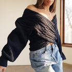 OKAKIE black cable knit sweater with a criss-cross off-shoulder neckline and wide dolman sleeves on a model