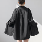 Back view of a woman wearing an OKAKIE black cotton poplin boyfriend over-shirt with a loose fit and tunic length.