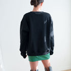 Back view of a model wearing an OKAKIE black cotton fleece sweatshirt with a relaxed fit and ribbed hem.