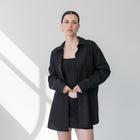 Model wearing an OKAKIE black cotton poplin boyfriend over-shirt with a tailored collar and button-up front.