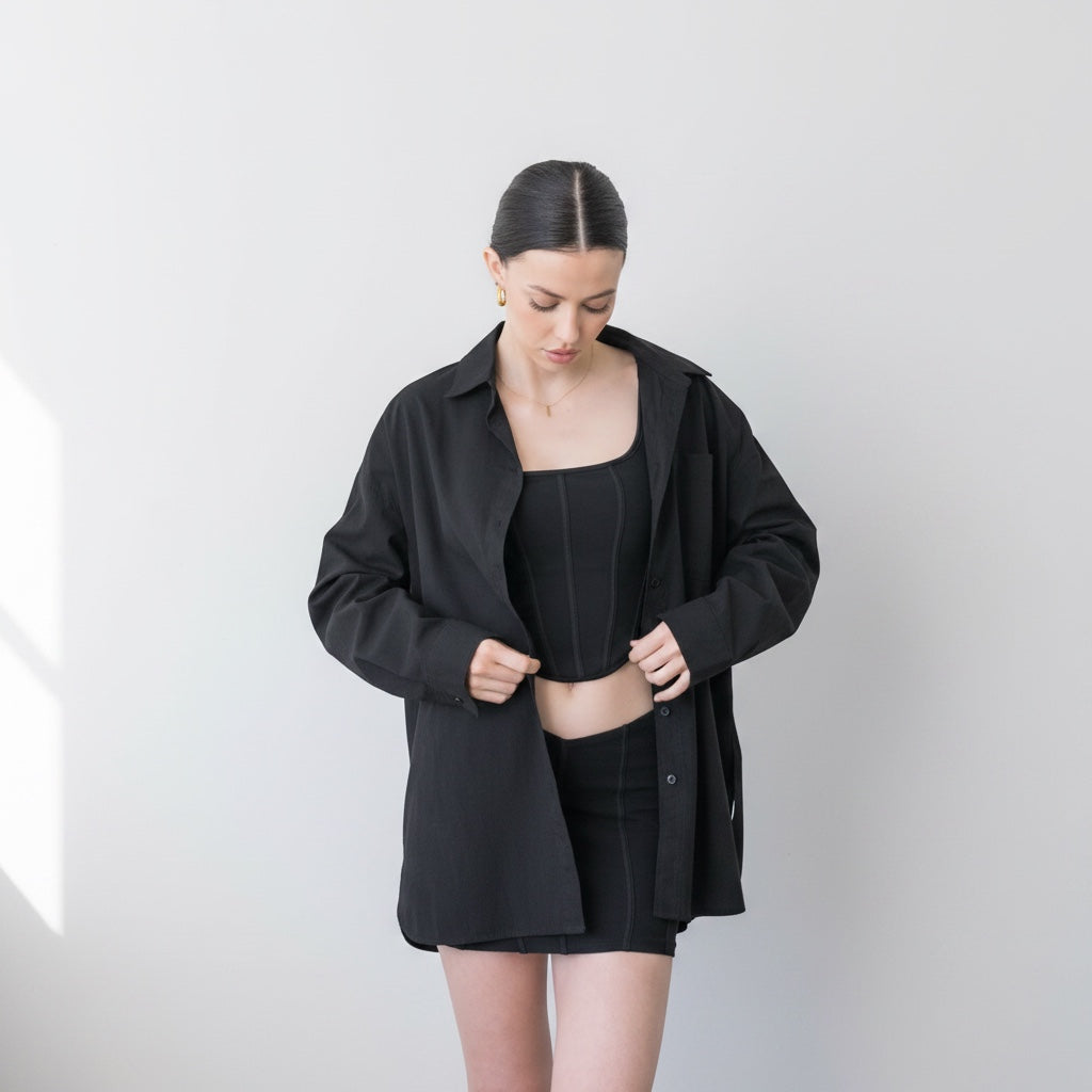 OKAKIE black cotton poplin boyfriend over-shirt worn open over a matching black corset top and mini skirt