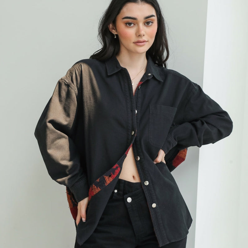 Model wearing an OKAKIE black cotton shacket with Southwestern-inspired patterned lining and snap-button closure.