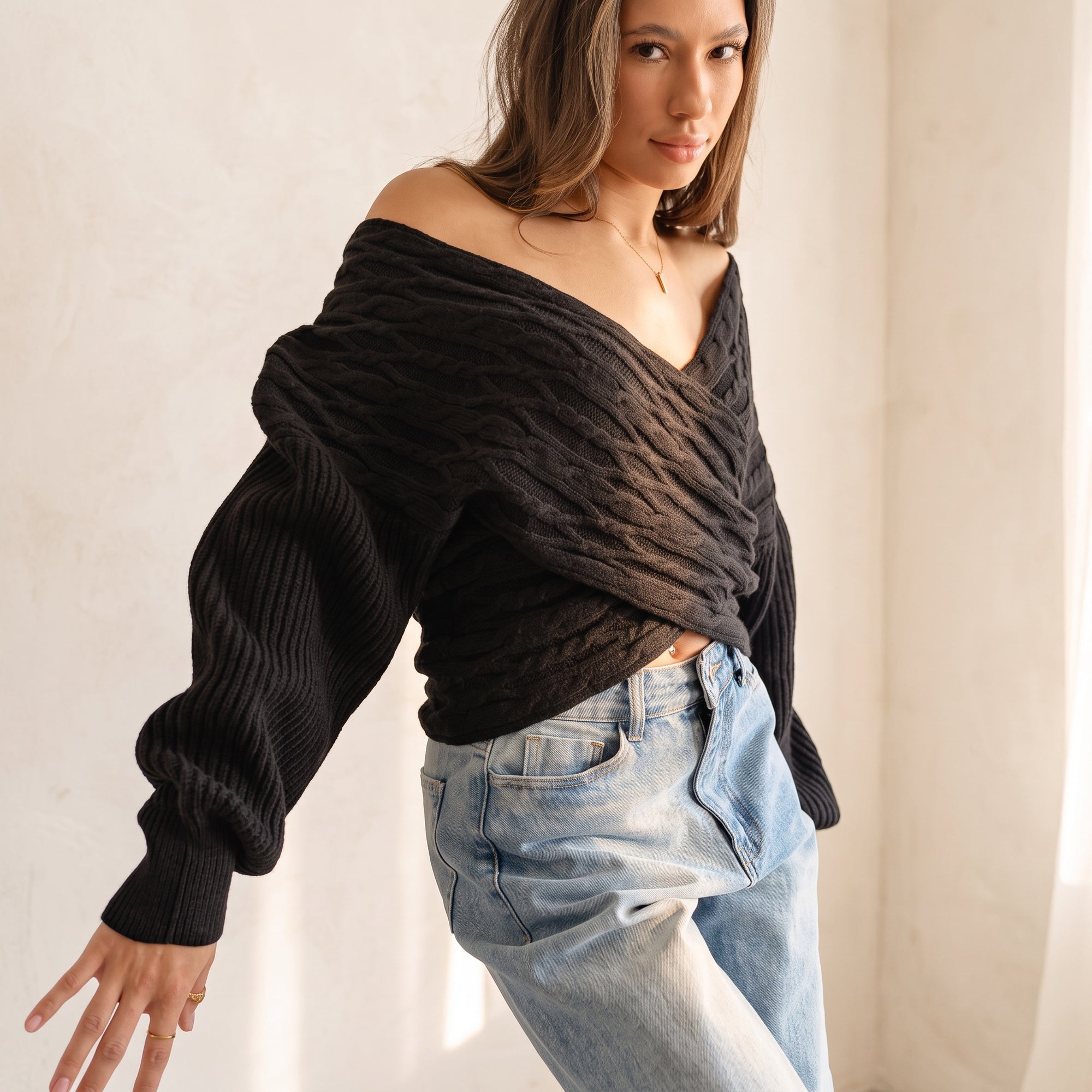 OKAKIE black cable knit sweater with a criss cross V-neckline and wide dolman sleeves worn off-shoulder