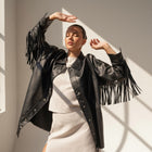 OKAKIE black vegan leather shacket featuring long fringe sleeves and silver snap buttons worn by a model in sunlight.