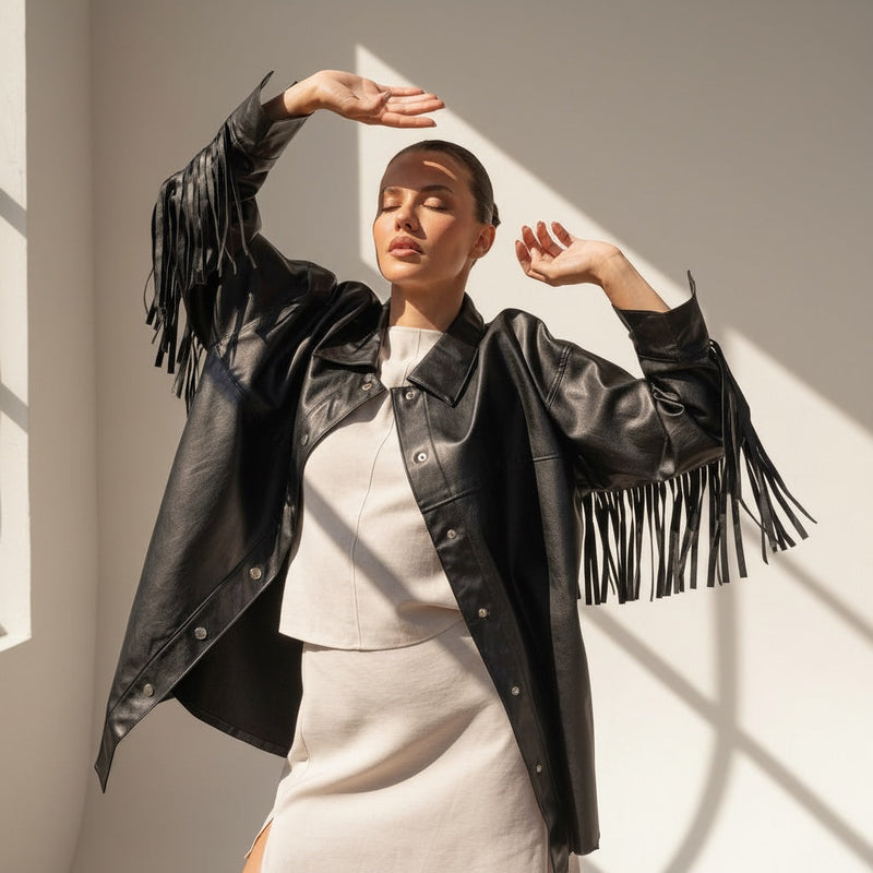 OKAKIE black vegan leather shacket featuring long fringe sleeves and silver snap buttons worn by a model in sunlight.