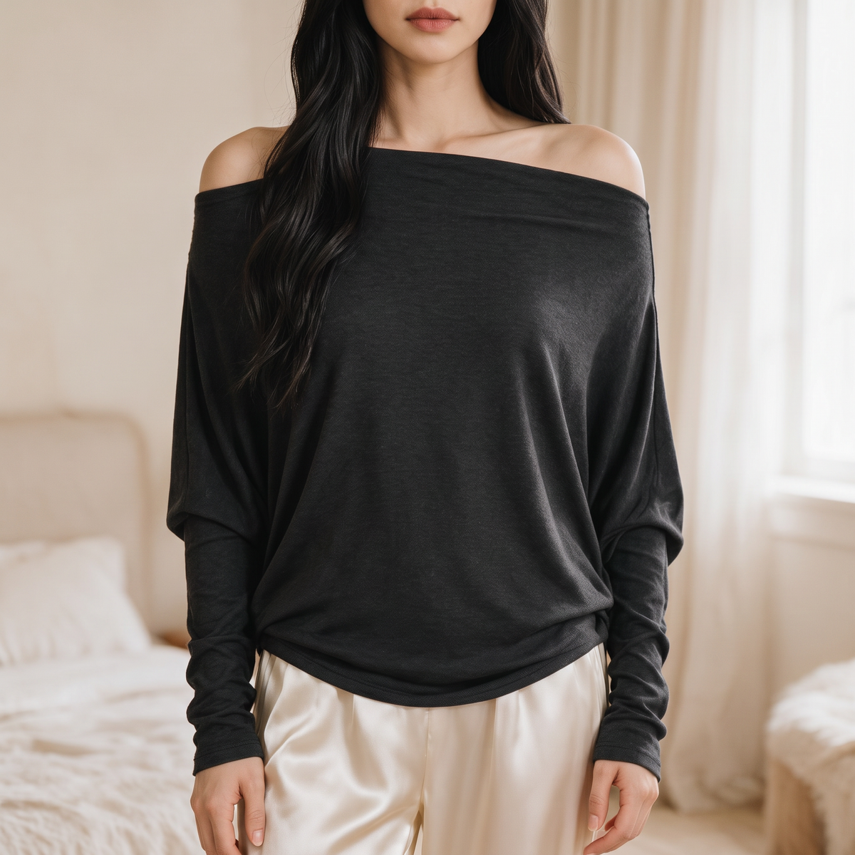 OKAKIE Maëlle black hacci knit top with a wide boat neckline worn off-shoulder, featuring relaxed dolman sleeves.