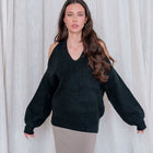 Model wearing OKAKIE black knit sweater with open shoulders and long sleeves, styled with a neutral skirt.