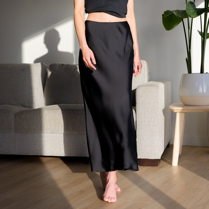 OKAKIE Serène matte black satin maxi skirt with a fluid silhouette and minimalist waistband worn by a model.