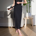 OKAKIE black midi wrap skirt in soft modal-blend knit with an adjustable waist tie, worn in a bright living room.