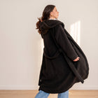 OKAKIE black plush teddy maxi robe coat with a hood and waist belt worn by a woman in a bright studio setting