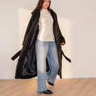 Model wearing an OKAKIE black plush teddy maxi robe coat with a shawl collar over a white top and wide-leg jeans.