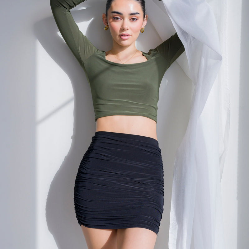 OKAKIE black ruched knit mini skirt worn by a model in a long-sleeve olive top against a white wall