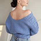 Model wearing an OKAKIE blue cable knit sweater with an off-shoulder design and wide dolman sleeves