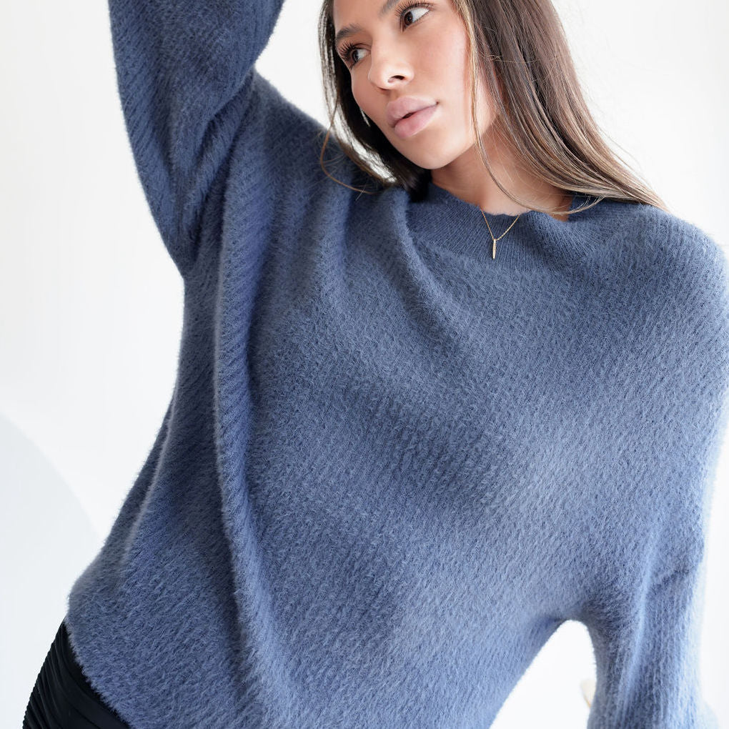 OKAKIE model wearing a fuzzy blue mock-neck tunic with long sleeves and a relaxed, soft knit texture.