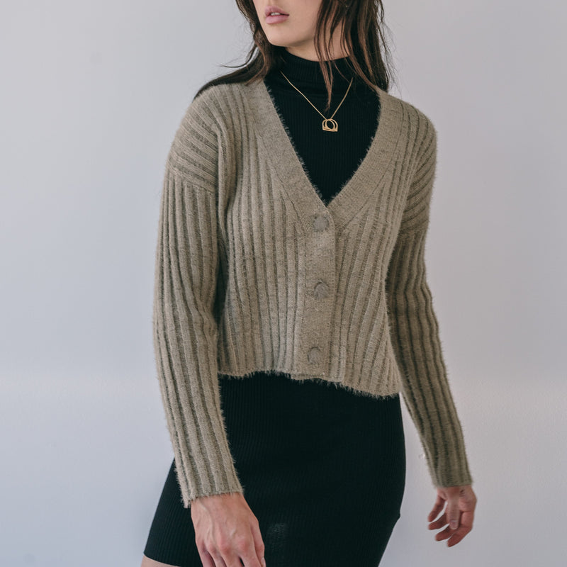 OKAKIE Elodie fuzzy ribbed cardigan in bronze featuring a V-neck, button front, and cropped fit over a black dress.