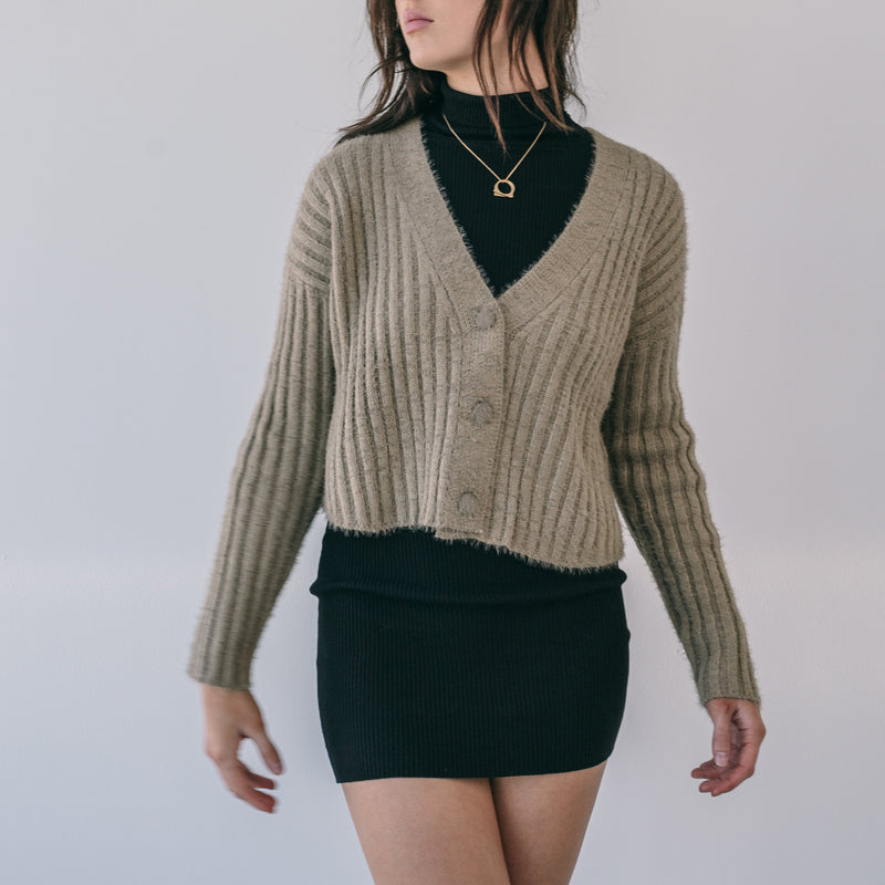 OKAKIE Elodie fuzzy ribbed cardigan in bronze worn over a black dress with a deep V-neck and button-front closure