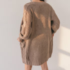 OKAKIE medium weight brown cable knit cardigan with drop shoulders, oversized pockets, and a loose thigh-length fit.
