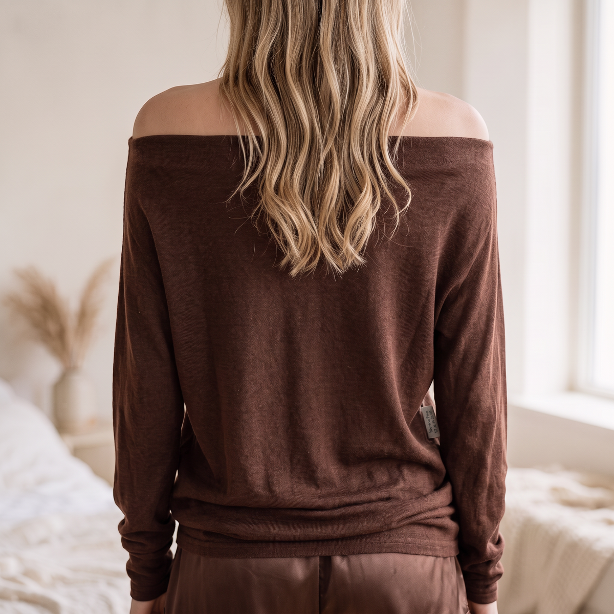 Back view of OKAKIE Maëlle draped hacci knit top in brown with off-shoulder boat neckline and long dolman sleeves.