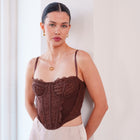 Model wearing OKAKIE brown lace corset top with contoured bust cups, spaghetti straps, and pointed front hem.
