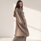 Model wearing an OKAKIE heavy warm brown purl knit cardigan with long sleeves and front pockets in a sunlit studio.