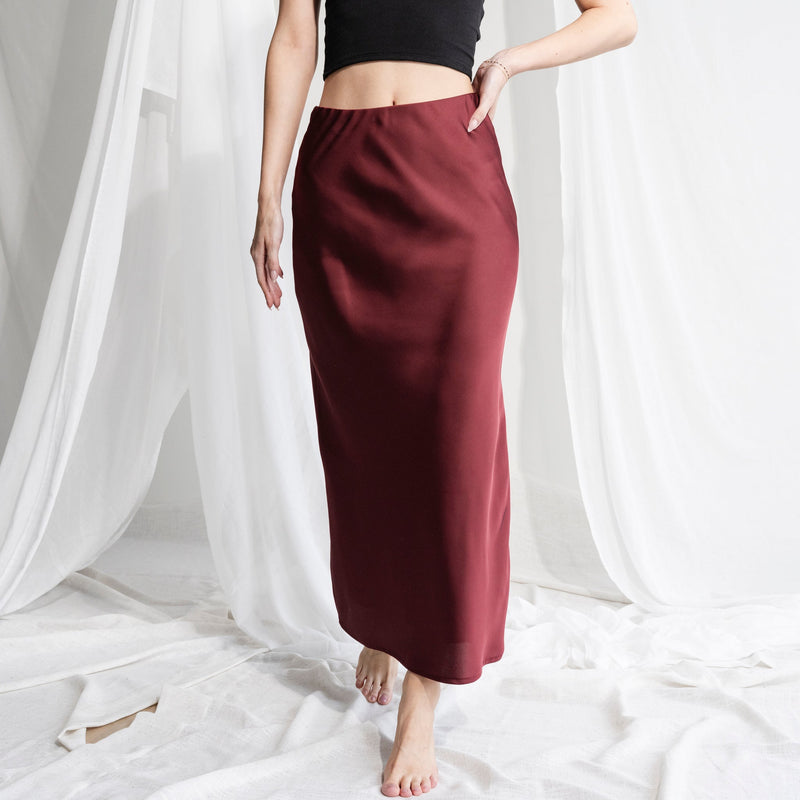 OKAKIE burgundy matte satin maxi skirt with a smooth waistband and fluid silhouette worn with a black crop top.