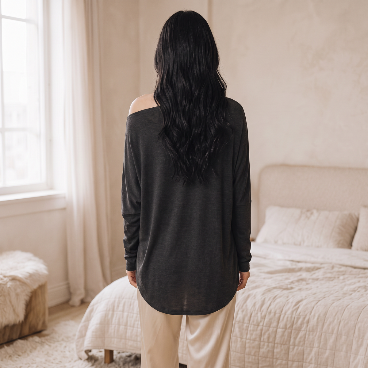 OKAKIE charcoal grey hacci knit top with a wide boat neckline and relaxed dolman sleeves worn in a bedroom setting