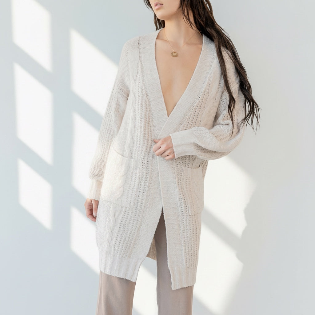 Model wearing an OKAKIE cream cable knit cardigan with a collarless design, drop shoulders, and oversized pockets.