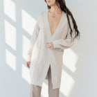 Model wearing an OKAKIE cream cable knit cardigan with a collarless design, drop shoulders, and oversized pockets.