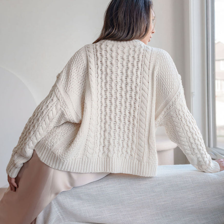OKAKIE cream oversized cable knit cotton sweater with dropped shoulders and ribbed hem worn by a woman