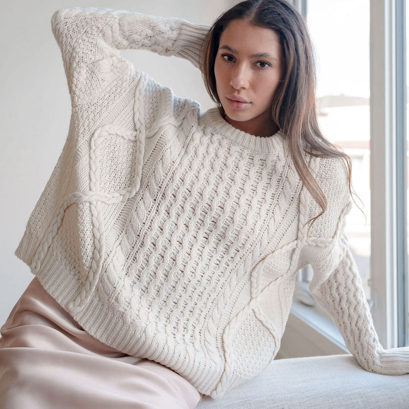 OKAKIE cream oversized cable knit cotton sweater with crew neck and dropped shoulders worn by a woman