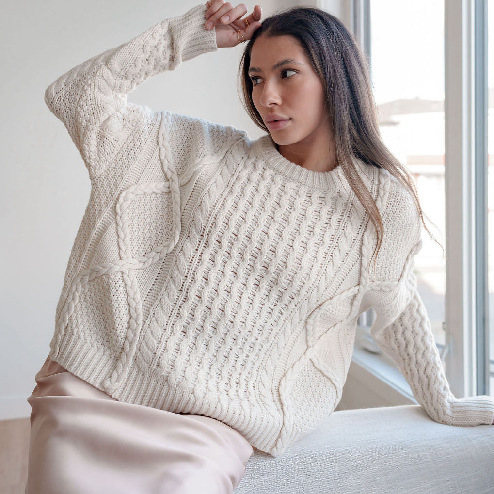 Model wearing an OKAKIE cream heavyweight cotton cable-knit sweater with a relaxed oversized fit and crew neckline.