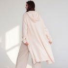 OKAKIE cream hooded maxi cardigan in a thick purl knit texture with oversized pockets, worn by a model from behind.
