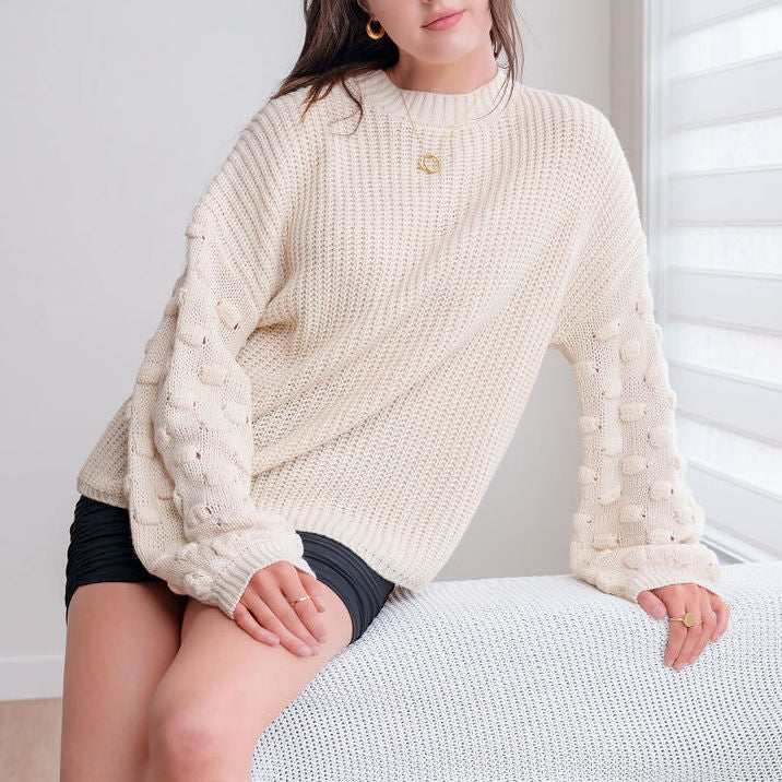OKAKIE cream popcorn sleeve knit sweater with a crew neckline and relaxed drop shoulders worn by a woman.