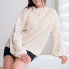 OKAKIE cream knit sweater featuring a ribbed body and dimensional popcorn-textured sleeves with a crew neckline.