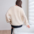 Back view of a woman wearing an OKAKIE cream popcorn sleeve knit sweater with a ribbed body and drop shoulders.