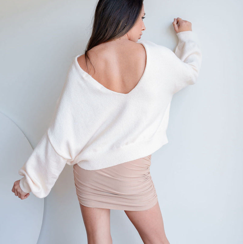 OKAKIE The Célene cream reversible sweater with a dramatic low back, worn with a beige ruched mini skirt