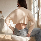 OKAKIE cream ribbed crop sweater with high neckline and long sleeves worn by a model in a sunlit room