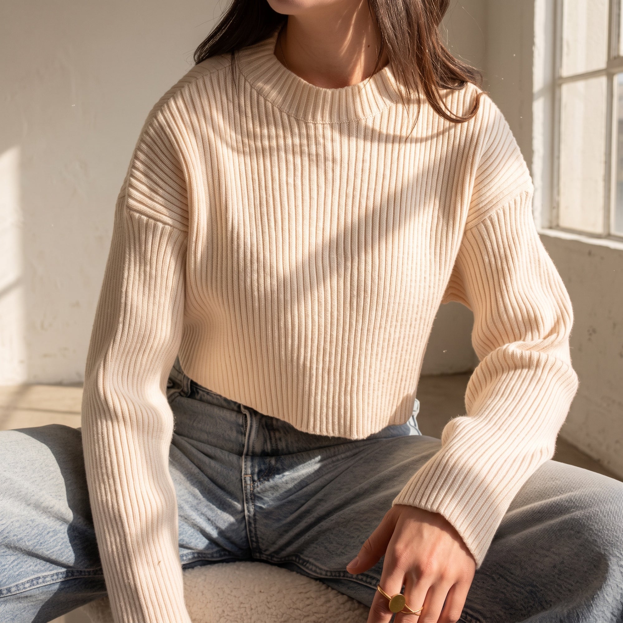 OKAKIE cream ribbed crop sweater with high neckline and long sleeves worn with blue jeans in a sunlit room