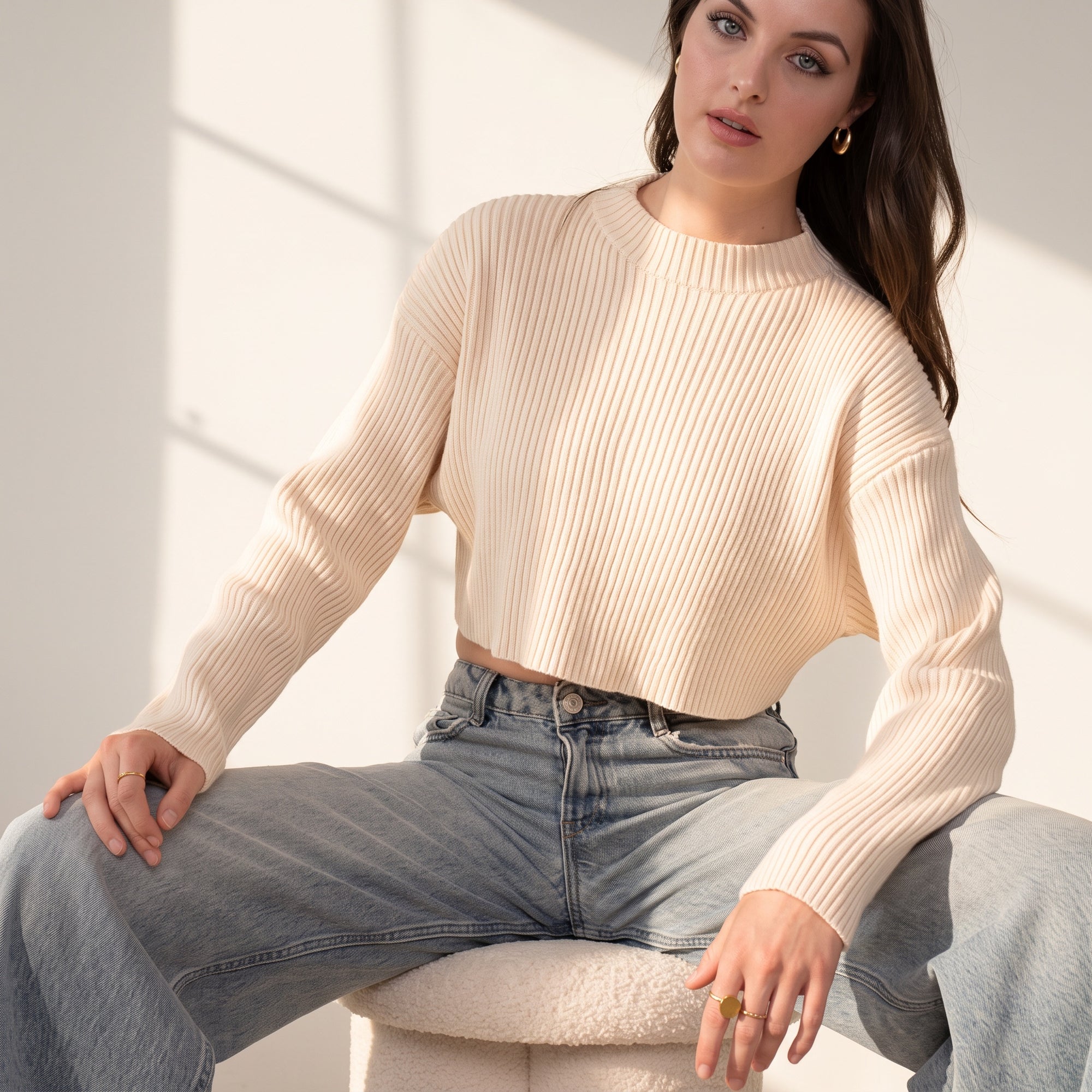 OKAKIE model wearing a cream-colored cropped ribbed sweater with a high neckline and long sleeves, paired with jeans.