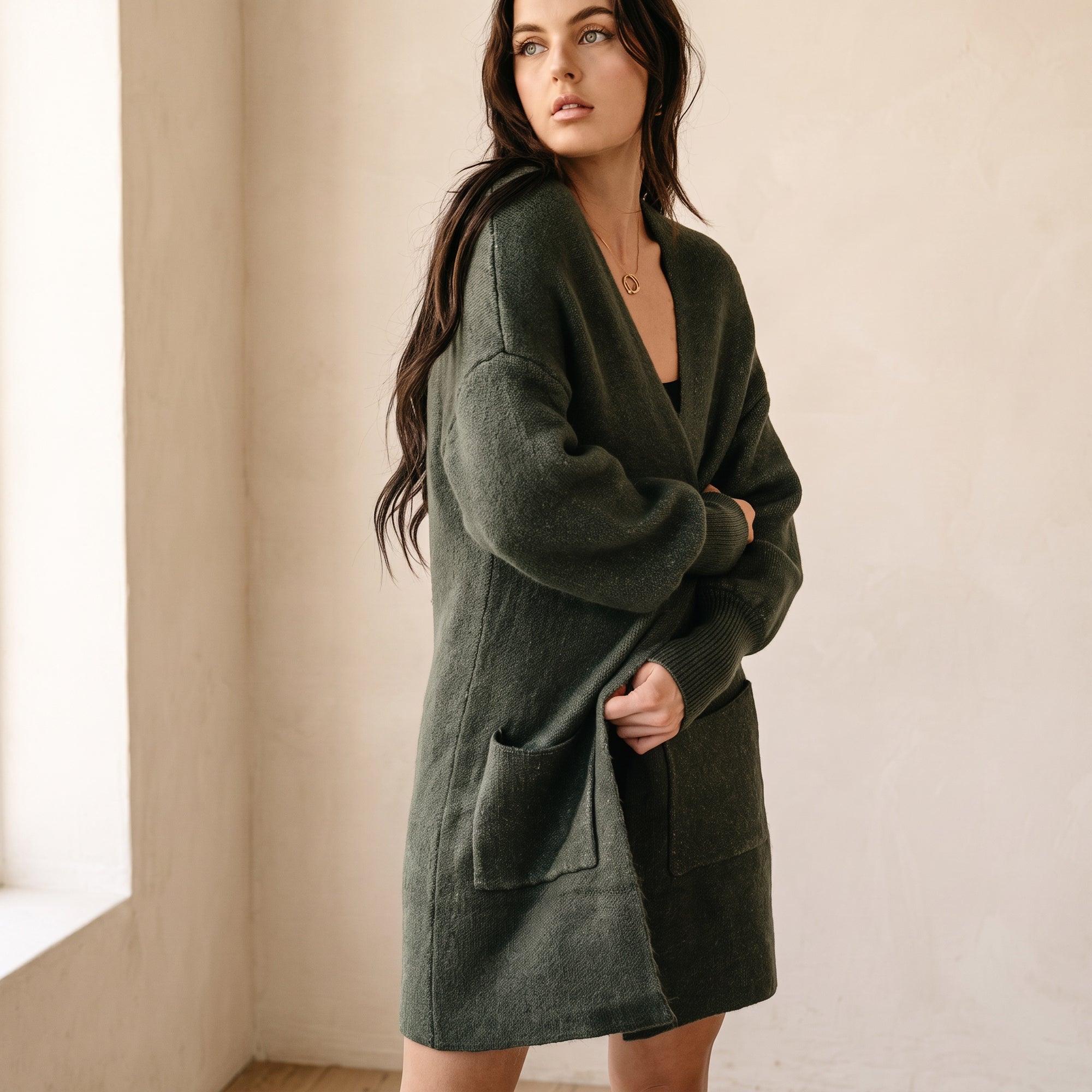 Model wearing an OKAKIE dark green marled knit structured cardigan with drop shoulders and oversized patch pockets.